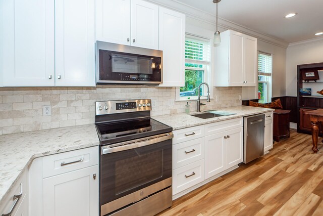 kitchen with crown molding, light wood-type flooring, decorative light fixtures, stainless steel appliances, and sink