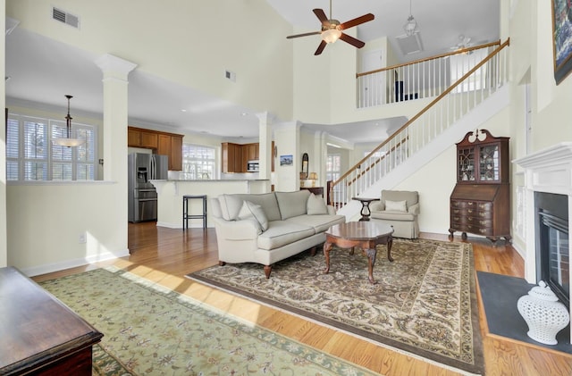 living area featuring a fireplace with flush hearth, visible vents, ornate columns, and wood finished floors