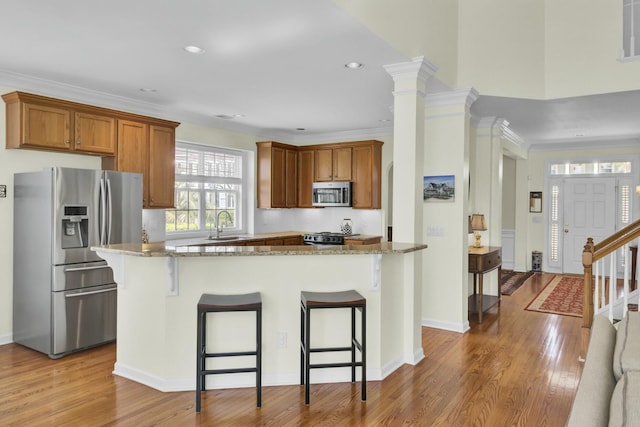 kitchen with light wood finished floors, brown cabinets, a kitchen breakfast bar, light stone countertops, and stainless steel appliances