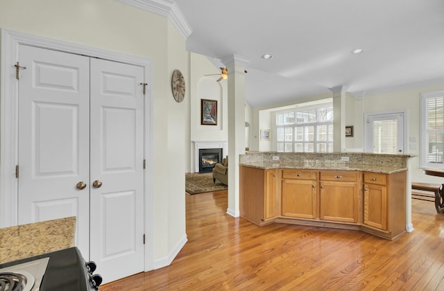 kitchen with lofted ceiling, light wood-style flooring, brown cabinetry, a glass covered fireplace, and light stone countertops