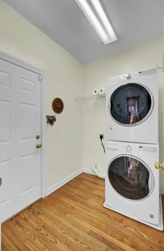 clothes washing area featuring laundry area, light wood-type flooring, stacked washing maching and dryer, and baseboards