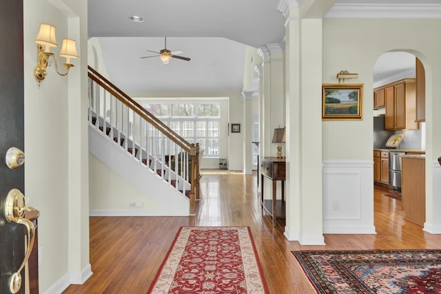 foyer entrance featuring arched walkways, stairway, ornamental molding, wainscoting, and wood finished floors