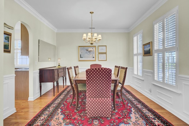 dining room with light wood-style flooring, ornamental molding, arched walkways, and a notable chandelier