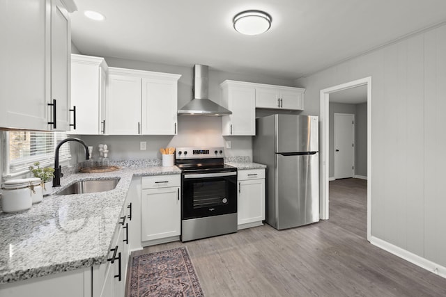 kitchen with light stone countertops, appliances with stainless steel finishes, sink, wall chimney range hood, and white cabinetry