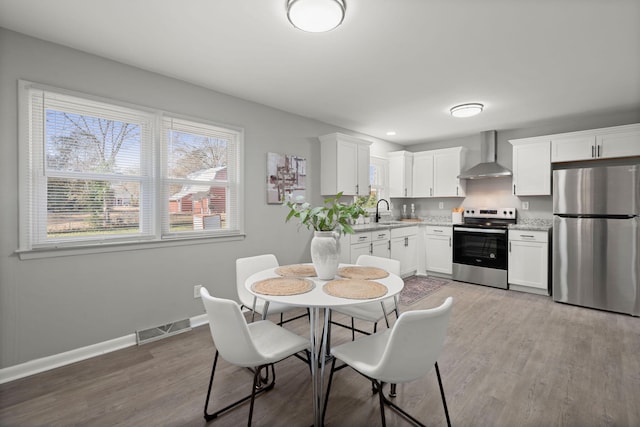 kitchen featuring appliances with stainless steel finishes, light hardwood / wood-style floors, white cabinetry, and wall chimney range hood