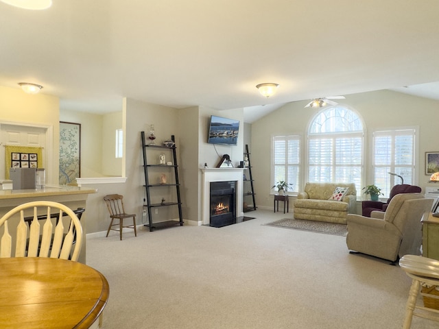 carpeted living room with lofted ceiling, a fireplace with flush hearth, baseboards, and a ceiling fan