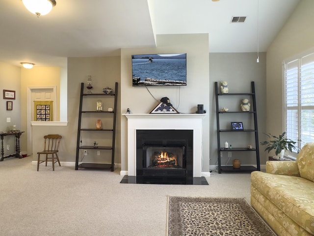 carpeted living area featuring a fireplace with flush hearth, visible vents, and baseboards