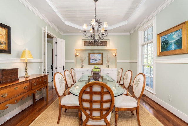 dining space with crown molding, a notable chandelier, hardwood / wood-style flooring, and a raised ceiling