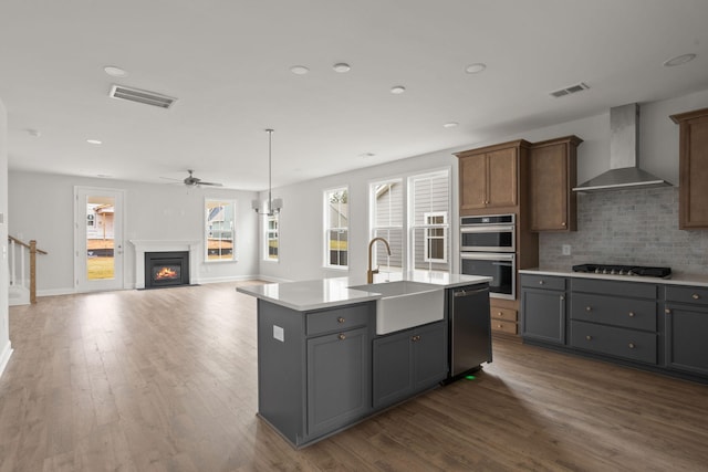 kitchen featuring wall chimney range hood, gray cabinets, sink, a kitchen island with sink, and stainless steel appliances