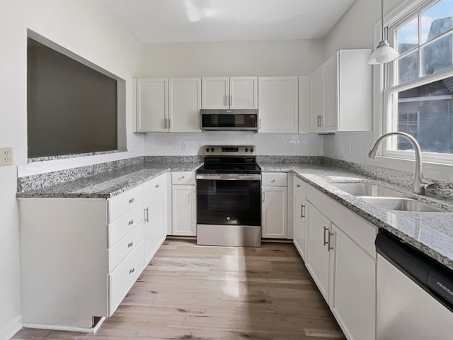 kitchen with sink, white cabinets, hanging light fixtures, light hardwood / wood-style flooring, and appliances with stainless steel finishes