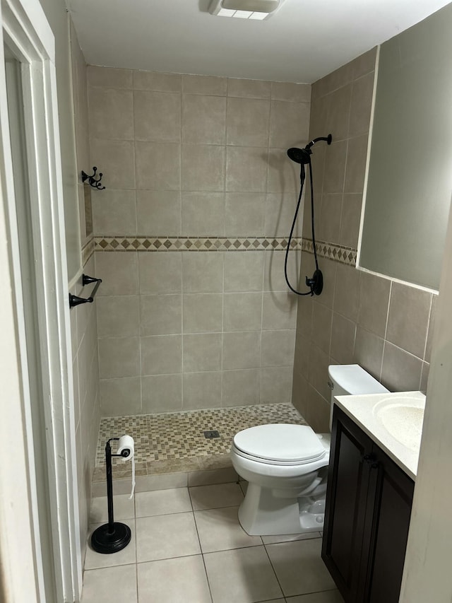 bathroom with toilet, a tile shower, tile walls, tile patterned floors, and vanity