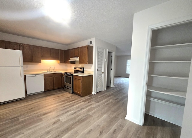 kitchen featuring light wood-type flooring, a textured ceiling, white appliances, and sink