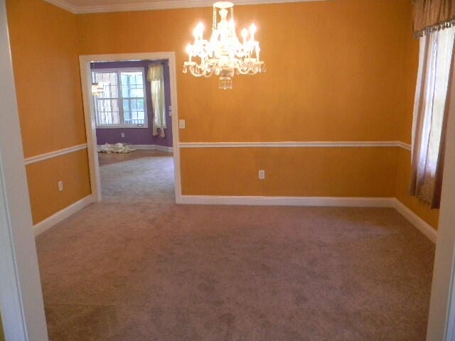 spare room featuring an inviting chandelier, carpet, and crown molding