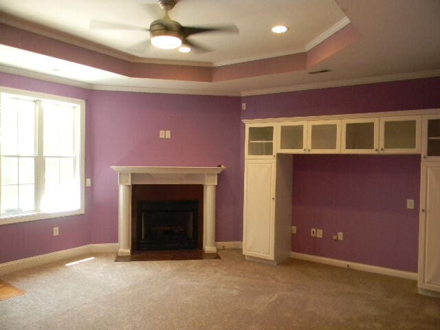 unfurnished living room featuring crown molding, carpet, ceiling fan, and a raised ceiling