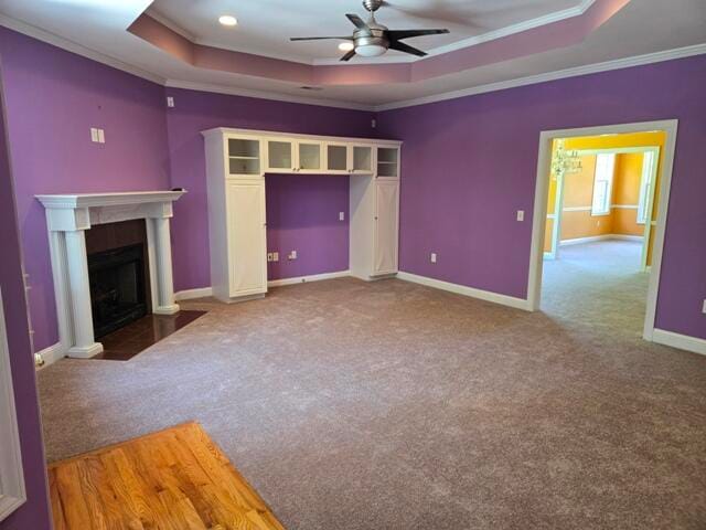 unfurnished living room featuring a raised ceiling, ceiling fan, carpet, and ornamental molding