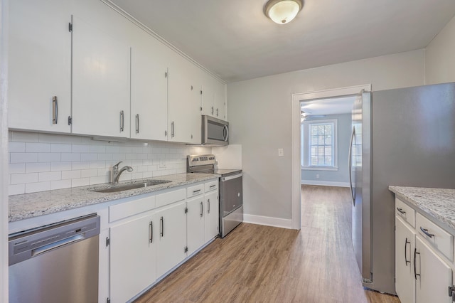 kitchen featuring tasteful backsplash, stainless steel appliances, light wood-type flooring, white cabinetry, and a sink