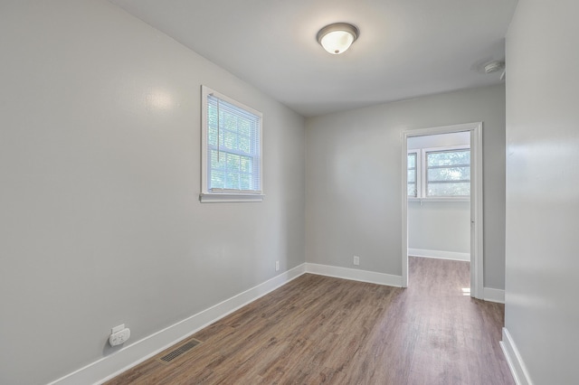 empty room with dark wood-style flooring, a healthy amount of sunlight, visible vents, and baseboards