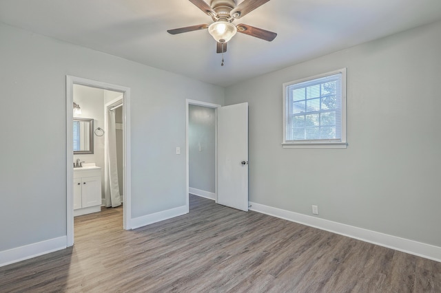 unfurnished bedroom with a sink, ensuite bath, baseboards, and wood finished floors