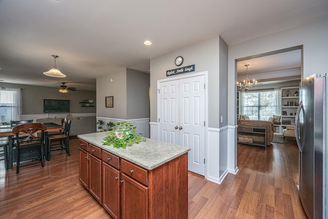 kitchen featuring stainless steel fridge, decorative light fixtures, ceiling fan with notable chandelier, light stone counters, and a center island