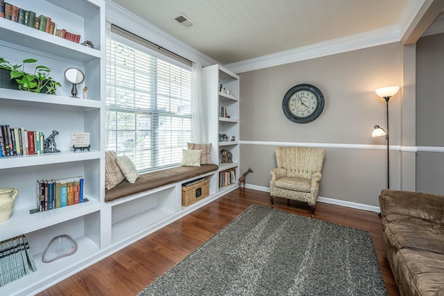 sitting room with dark wood-type flooring, crown molding, and built in shelves