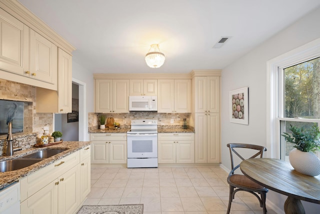 kitchen featuring white appliances, backsplash, stone counters, sink, and cream cabinetry