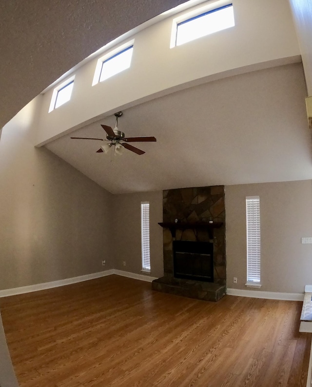 unfurnished living room with ceiling fan, a fireplace, a towering ceiling, and hardwood / wood-style flooring