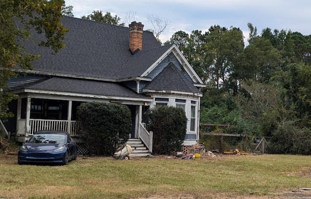 view of front of house featuring roof with shingles, a front lawn, a chimney, and a porch