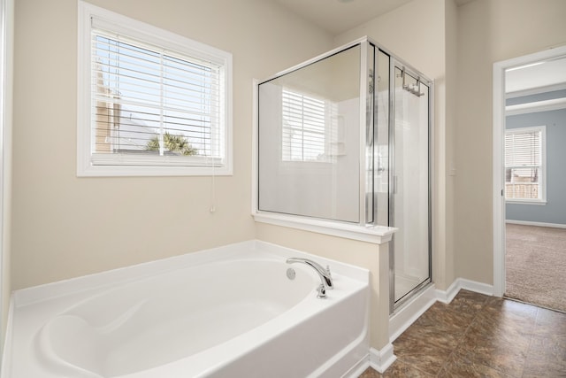 full bathroom featuring a stall shower, a healthy amount of sunlight, a garden tub, and baseboards