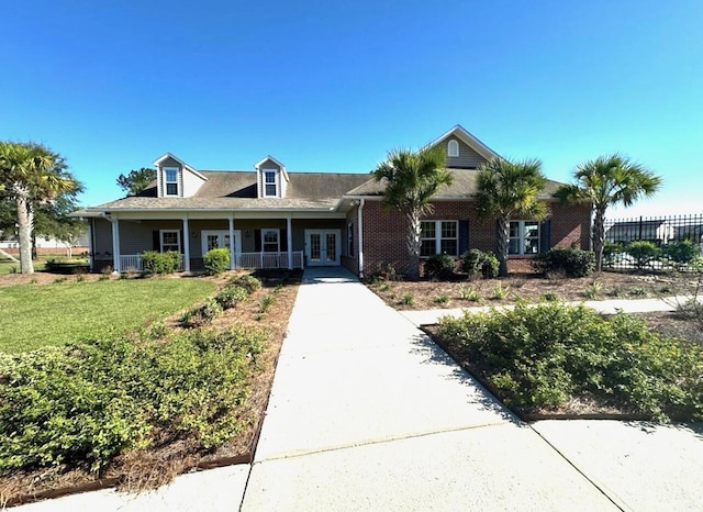 view of front of property with covered porch, brick siding, fence, french doors, and a front yard