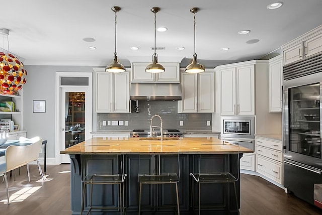 kitchen with dark hardwood / wood-style flooring, pendant lighting, a center island with sink, butcher block countertops, and stainless steel microwave