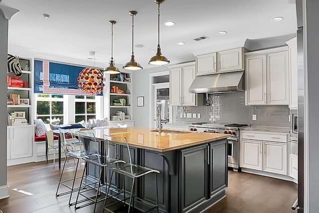 kitchen with a kitchen breakfast bar, high end stainless steel range oven, dark hardwood / wood-style floors, an island with sink, and decorative light fixtures