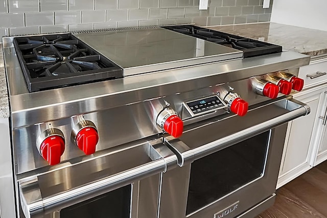 details featuring light stone countertops, dark hardwood / wood-style flooring, tasteful backsplash, range with two ovens, and white cabinetry