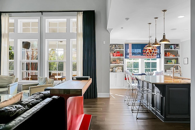 interior space featuring dark hardwood / wood-style flooring, a breakfast bar, sink, decorative light fixtures, and a center island with sink