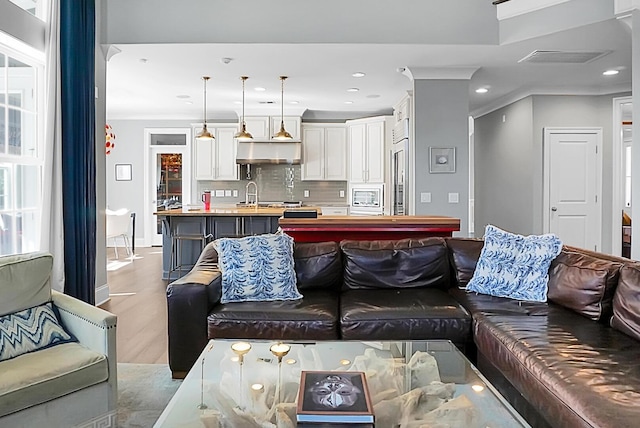 living room featuring crown molding, sink, and light hardwood / wood-style floors