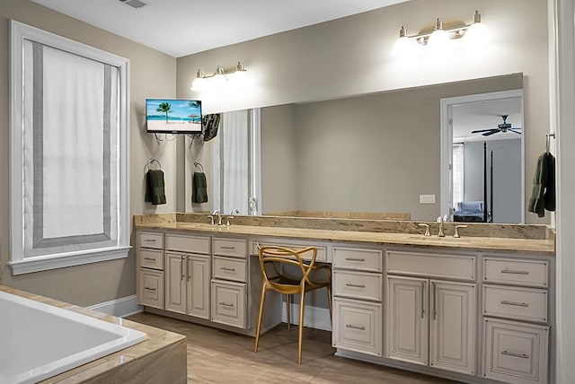 bathroom with a relaxing tiled tub, vanity, and ceiling fan