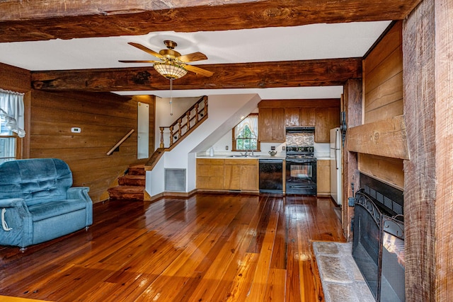 unfurnished living room with ceiling fan, wood walls, sink, beam ceiling, and dark hardwood / wood-style flooring