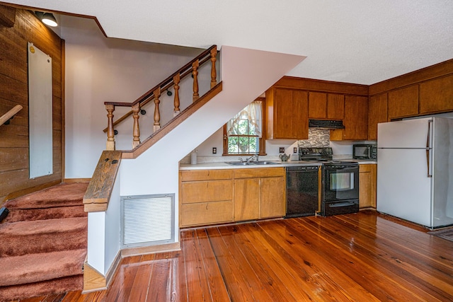 kitchen featuring dark wood-type flooring, sink, range hood, wooden walls, and black appliances