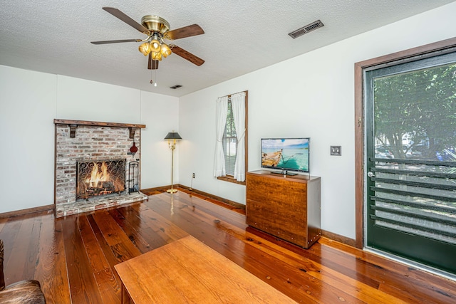 living room with ceiling fan, a textured ceiling, a brick fireplace, and hardwood / wood-style floors