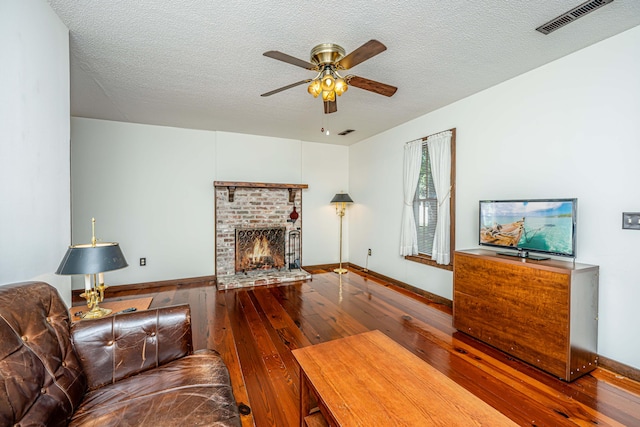 living room featuring a brick fireplace, ceiling fan, hardwood / wood-style floors, and a textured ceiling