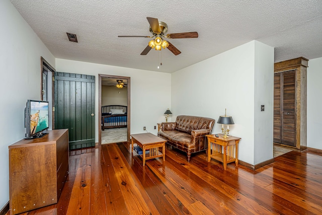 living room featuring ceiling fan, a textured ceiling, and dark wood-type flooring