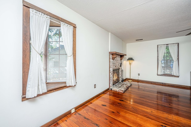 interior space with a brick fireplace, a textured ceiling, hardwood / wood-style floors, and ceiling fan