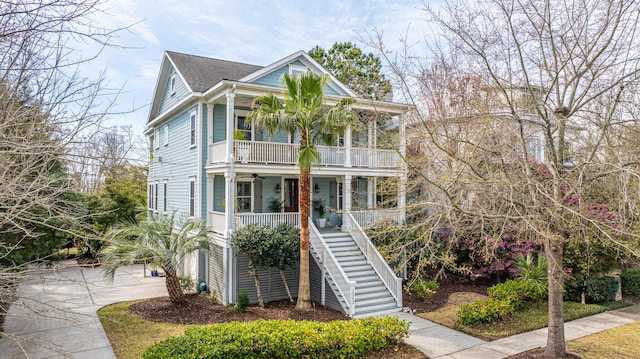 coastal home with ceiling fan, a porch, stairs, a balcony, and driveway