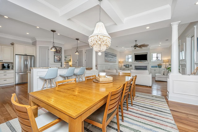 dining space with wood finished floors, a wainscoted wall, ornate columns, beam ceiling, and ceiling fan with notable chandelier