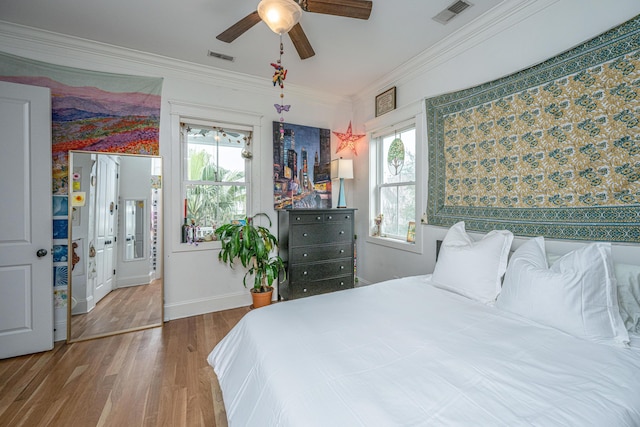 bedroom featuring baseboards, wood finished floors, visible vents, and ornamental molding