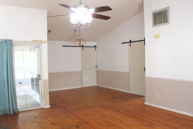 unfurnished room featuring ceiling fan with notable chandelier, a barn door, wood-type flooring, and vaulted ceiling