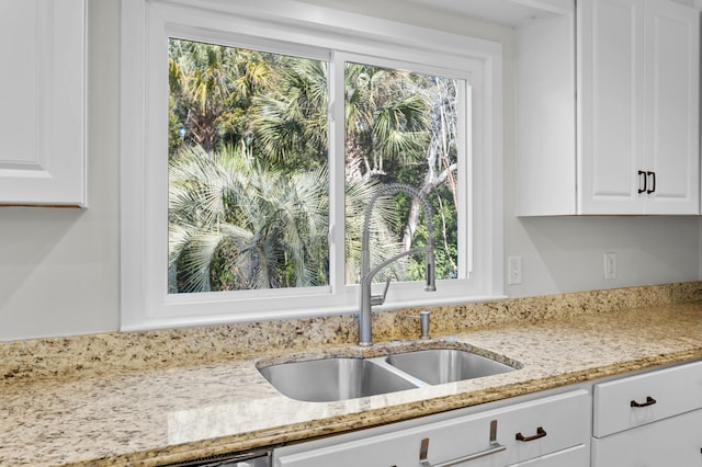 kitchen featuring white cabinets, light stone counters, and a sink