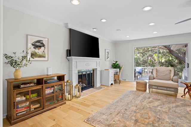 living room featuring recessed lighting, light wood-style floors, a fireplace with raised hearth, and crown molding