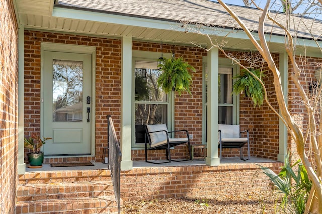 entrance to property with brick siding, a porch, and a shingled roof