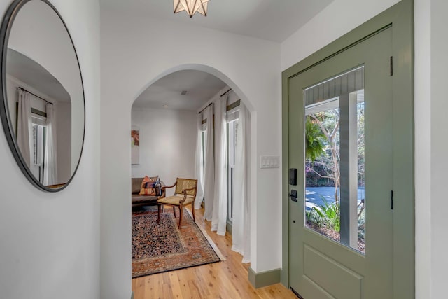 entryway with arched walkways, baseboards, and light wood-style floors