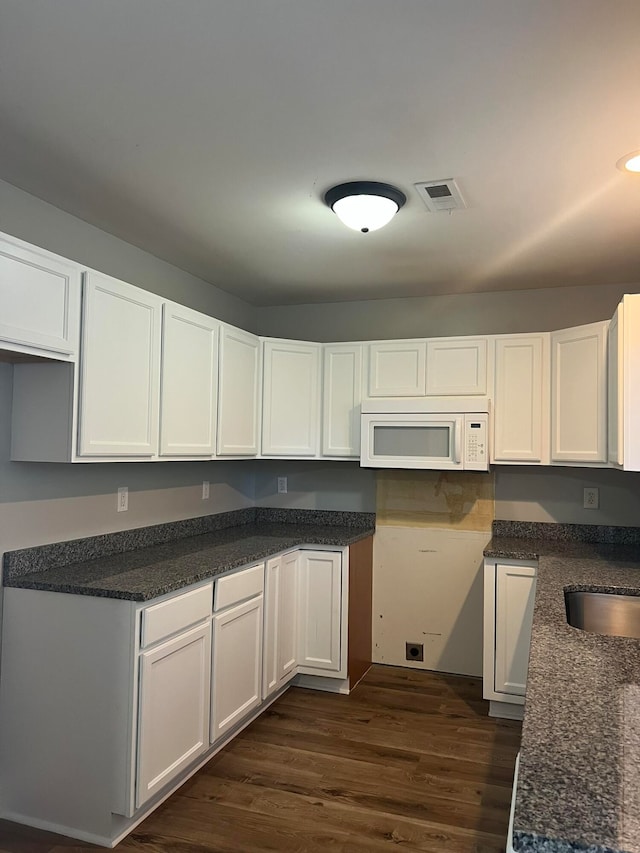 kitchen featuring white cabinets, dark stone counters, dark hardwood / wood-style floors, and sink